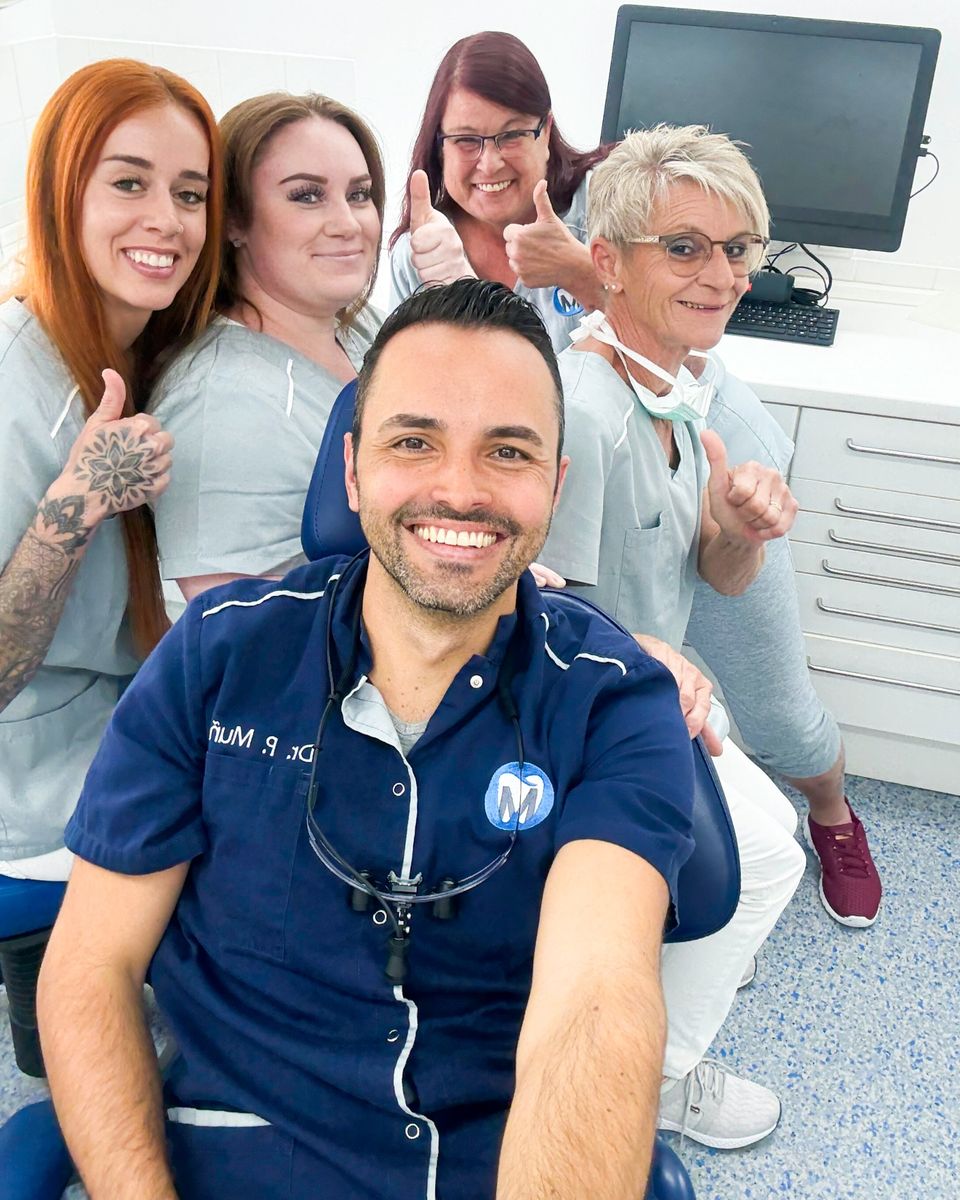 Dr. Pablo Muñoz mit seinem Praxisteam im Behandlungszimmer – alle lächeln und zeigen den Daumen nach oben